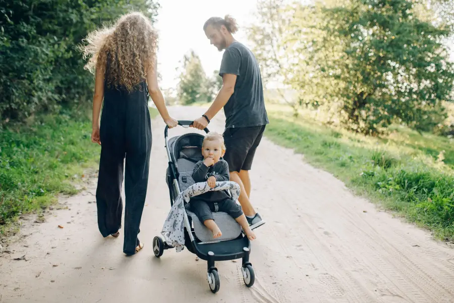 Perhe kävelee puistopolulla ja lapsi istuu rattaissa